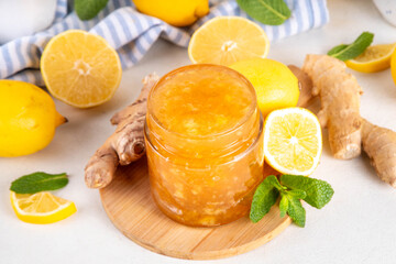 Ginger lemon jam marmalade preserves in small jar with fresh ginger, lemons and mint, on white table copy space
