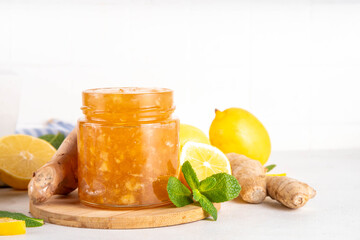 Ginger lemon jam marmalade preserves in small jar with fresh ginger, lemons and mint, on white table copy space