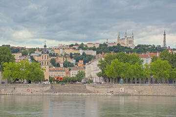 Fototapeta premium Houses and trees along river Rhone, with Basilica of Notre-Dame de Fourvière on a hill in Lyon, France 