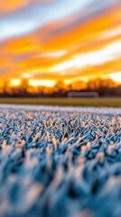A close-up of a grass field with a dramatic, colorful sunset in the background. The sky is filled with vibrant orange and yellow hues.