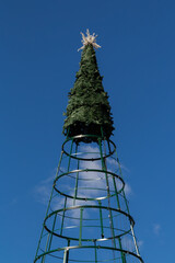 The Christmas tree stands tall with a bright star on top, while a light cloud moves across the blue sky behind it.