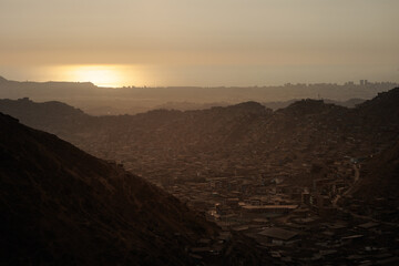Hillside shantytown contrasting with a distant modern city skyline in the mist, illustrating social inequality, poverty, and urban sprawl in Lima, Peru