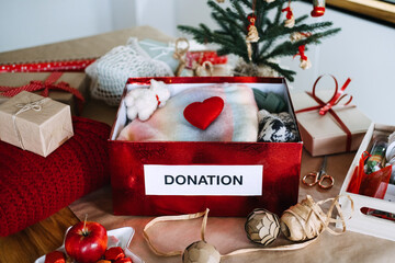 Red box labeled DONATION filled with soft items and heart sits on table surrounded by gifts and...