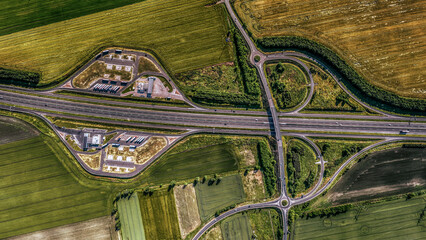 Top-down aerial view of a highway interchange with service area and farmland. Clean geometry and...