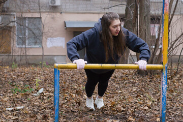 Obraz premium At an urban fitness park, a person in casual sportswear dips between yellow parallel bars. Elbows are bent sharply, showing the lowest phase of the dip exercise outdoors