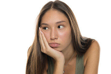 Fototapeta premium Studio shot of young woman with long brown hair wearing green tank top, resting her face on hand and looking bored, on white background.