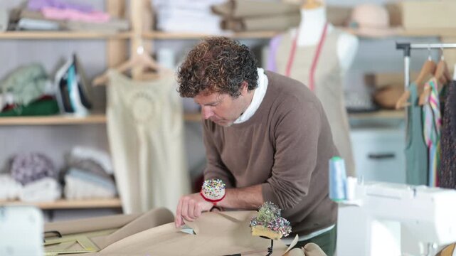  Adult male tailor cutting out pattern from paper with scissors in sewing workshop