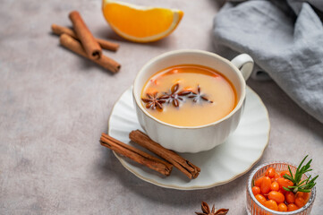 Sea buckthorn herbal tea in a cup on a light background with orange, spices and berries