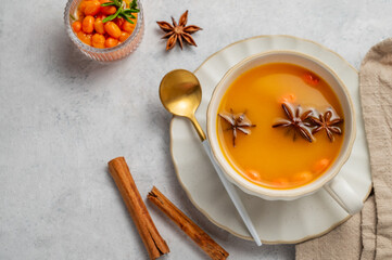 Sea buckthorn herbal tea in a cup on a light background with spices and berries.