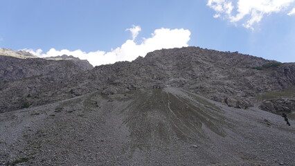 Dramatic steep rocky scree slope leading to a mountain summit beneath a bright blue sky, challenge concept.