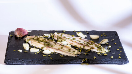 boquerones en vinagre con aceite de oliva ajo y perejil en un plato de pizarra negro