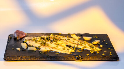 boquerones en vinagre con aceite de oliva ajo y perejil en un plato de pizarra negro