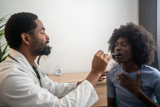 Male doctor carefully examining female patient’s throat in medical clinic during routine checkup