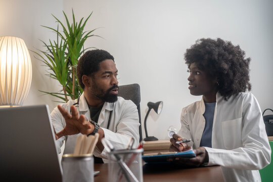 Two doctors, smiling, look at a laptop screen during a discussion in a modern office setting.