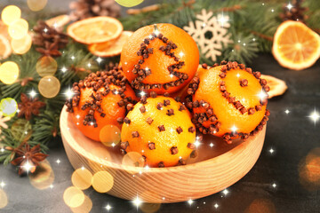 Fototapeta premium Fresh tangerines decorated with cloves (Pomander balls) and fir tree branches on table, bokeh lights