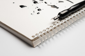 white spiral notebook with ink stains on the page and a black modern fountain pen. A stationery advertising background