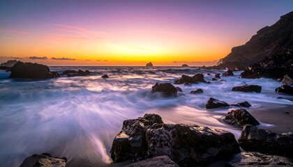 Fototapeta premium Vivid sunset colors meet the rocky shoreline, waves cascading over dark rocks with hill in the background