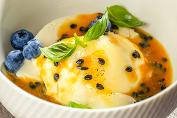 Exotic panna cotta dessert topped with vibrant passion fruit sauce, fresh blueberries and basil leaves,