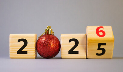 2026 New Year symbol. Businessman turns wooden cube and changes Year 2025 to 2026. Beautiful grey background with Christmas ball. Copy space. Business and 2026 happy new year concept