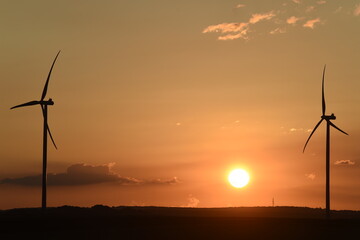 lever de soleil sur des &eacute;oliennes &agrave; contre-jour; ciel d&eacute;grad&eacute; couleur bleue et orange avec des petits nuages cumulus blancs gris et noirs