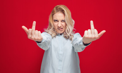 Young woman showing fuck off gesture, isolated on red background. Female person with obscene gesture giving the middle finger and looking to camera