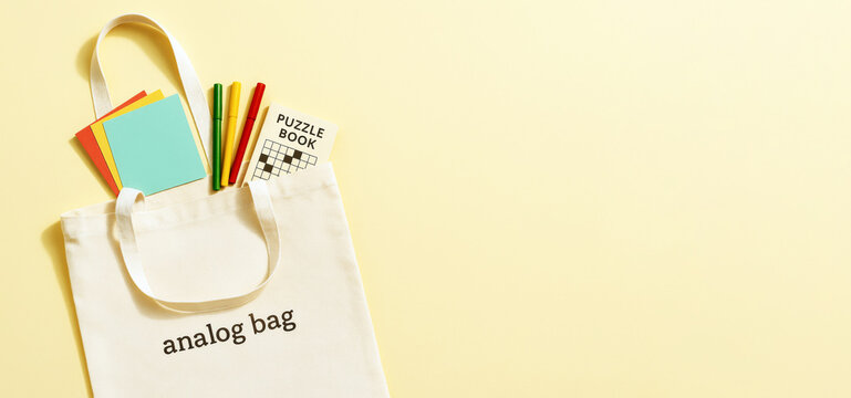 Analog bag with notebooks, puzzle book, and pens on yellow background