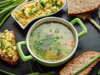 Fresh natural chicken bouillon with veggies and egg sandwiches for cold season to keep warm and get vitamins. Bowl portion with hot homemade chicken broth and baked whole wheat bread.