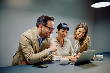 Diverse business colleagues working together on a project, analyzing data, and smiling while using a laptop during a office meeting