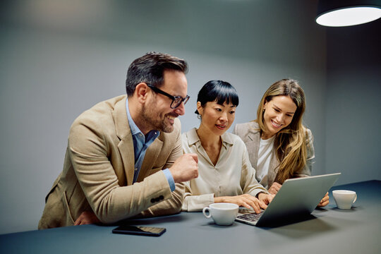 Diverse business colleagues working together on a project, analyzing data, and smiling while using a laptop during a office meeting