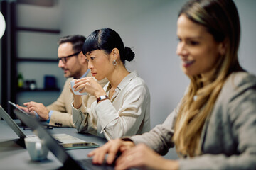 Diverse business people concentrating while working on laptops and drinking coffee during a meeting or collaborative work session