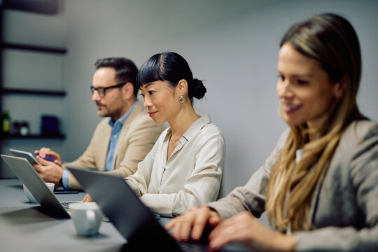 Diverse business professionals using laptops and tablets during an important meeting, focusing on tasks and teamwork in the office