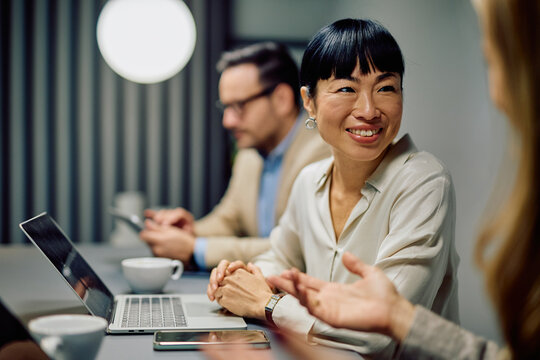 Asian business woman smiling, listening attentively to colleague during a professional office meeting, showing collaboration and discussion