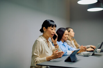 Asian businesswoman talking on mobile phone during a business meeting with diverse colleagues in a modern office