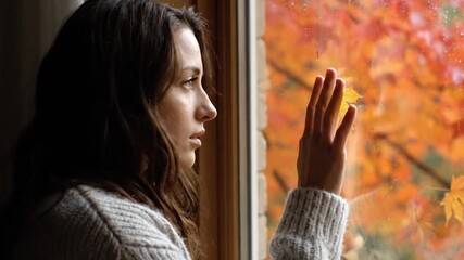 Thoughtful young woman looking out window, autumn leaves, fall season - Powered by Adobe