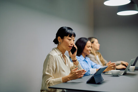 Asian businesswoman talking on mobile phone during a business meeting with diverse colleagues in a modern office