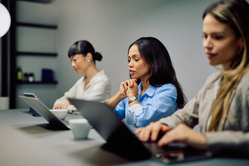 Diverse businesswomen concentrating on their laptops, attending a serious meeting or conference in a contemporary office environment