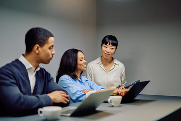Diverse business professionals having a meeting, discussing strategy while looking at a laptop and using a digital tablet