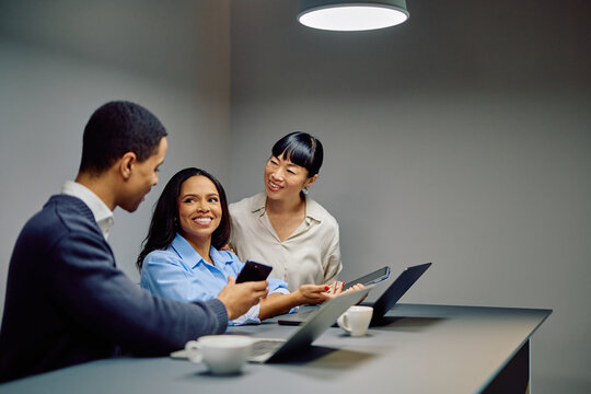 Three diverse business colleagues collaborating and sharing ideas, looking at a smartphone during an informal meeting in a modern office