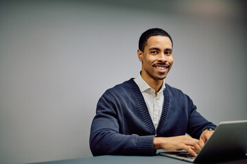 Happy African American businessman working remotely on a laptop, looking at the camera and smiling, representing success and professionalism