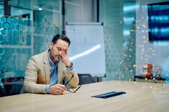 Stressed businessman sitting at a conference table with hand on his face, feeling overloaded and exhausted from work