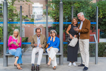 Mature friends connecting with smartphones at bus stop