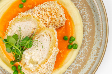 Crispy chicken roll served on creamy mashed potatoes with vibrant carrot pure and fresh green peas, top view