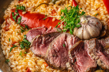 Gourmet paella with juicy medium-rare beef slices, roasted garlic and vegetables, rich Spanish rice close-up, top view food background