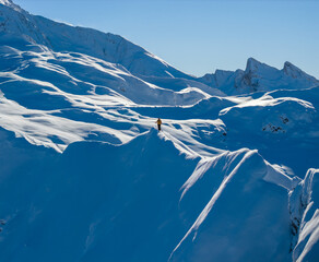 Aerial photo of a ski mountaineer standing on a snowy alpine ridge in Austria. Winter landscape, backcountry adventure, clear blue sky with sunshine and solitude in breathtaking mountain scenery.