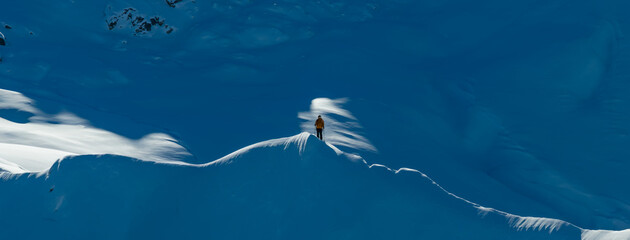 Aerial photo of a ski mountaineer standing on a snowy alpine ridge in Austria. Winter landscape, backcountry adventure, clear blue sky with sunshine and solitude in breathtaking mountain scenery.
