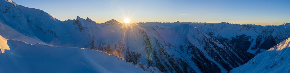 Panoramic view of the Austrian Alps at sunset. Snow-covered peaks glowing in warm evening light create a stunning high-resolution winter mountain landscape.