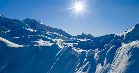 Aerial photo of a ski mountaineer standing on a snowy alpine ridge in Austria. Winter landscape, backcountry adventure, clear blue sky with sunshine and solitude in breathtaking mountain scenery.