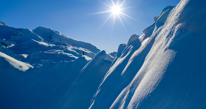Aerial photo of a ski mountaineer standing on a snowy alpine ridge in Austria. Winter landscape, backcountry adventure, clear blue sky with sunshine and solitude in breathtaking mountain scenery.