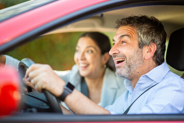 Excited couple driving red car and reacting with surprise and joy