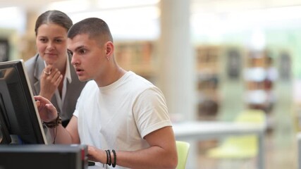 Female teacher helps boy find information on internet using computer in university library. High quality 4k footage - Powered by Adobe